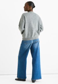 Gray knit sweater with a high neckline, loose fit, and ribbed hem paired with light blue wide-leg jeans and black shoes.