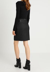 Svart långärmad topp med volangkrage, matchad med en knälång, texturerad svart kjol och svarta klackboots med nitar.