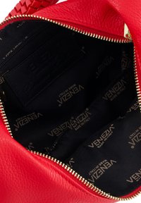 Innenansicht einer roten Ledertasche mit Reißverschluss, gefüttert mit schwarzem Stoff, der das Muster "Venezia Made in Italy" zeigt. Strukturierte Oberfläche.