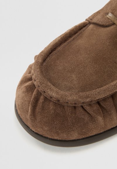 Brown suede slipper with gathered texture at the toe, rounded front, and a dark rubber sole. Hand-stitched detailing along the edge.