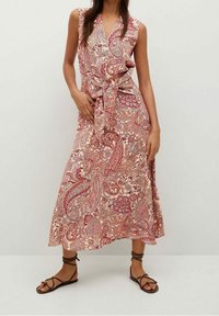 Robe longue en tissu à motifs complexes arborant un motif paisley rouge, rose et crème. Se noue à la taille, sans manches avec un décolleté en V.