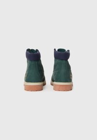 Stivali alla caviglia in pelle verde con colletto in tessuto blu navy, suola in gomma marrone chiaro e discreto dettaglio del logo sul lato. Design minimalista.