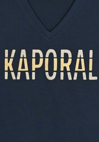 Námořnické V-krční tričko s kovově zlatým a stříbrným nápisem "KAPORAL" v tučném, blokovém stylu. Měkká tkanina s hladkým povrchem.