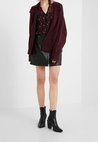 Mörkröd oversized kashmirblandad blazer, svart läderkjol med dragkedja, mönstrad blus med små detaljer, svarta spetsiga ankelskor med grova klackar.