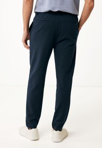 Pantaloni stretch blu con vestibilità affusolata, due tasche posteriori e polsini elastici. Indossati con sneakers bianche su uno sfondo neutro.