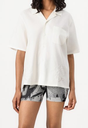 Personne portant une chemise blanche ample à manches courtes avec poche et un short ajusté noir et blanc à motifs.