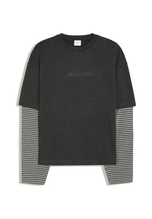 T-shirt noir à manches courtes superposé sur des manches longues gris et noir à rayures horizontales, avec un petit texte en pointillé "silent notes" sur la poitrine.