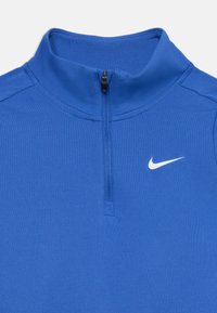 Sininen vetoketjullinen urheilupaita, joka on valmistettu sileästä kankaasta. Varusteena korkea kaulus ja valkoinen Nike-logo rinnassa.