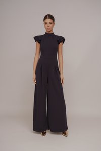 Tuta blu scuro con maniche corte a volant, colletto alto, pantaloni a gamba larga plissettati e superficie liscia. Completato da tacchi dorati.