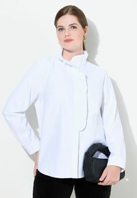 Camicia bianca a maniche lunghe con colletto arricciato e apertura con bottoni, abbinata a pantaloni neri e una borsa nera a trama.