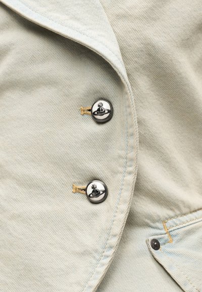 Φωτεινό μπεζ ύφασμα τζιν με δύο μεταλλικά κουμπιά που διαθέτουν σχέδιο υδρογείου και δαχτυλιδιού, μαζί με εμφανείς χρυσές και μπλε ραφές.