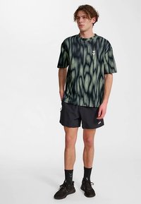 Kortärmad skjorta i svart och olivfärgat tie-dye-mönster, gjord av mjukt tyg. Bärs med svarta shorts och sneakers, med diskreta logotyper.