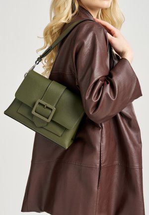 Borsa a tracolla in pelle verde oliva con una forma strutturata, caratterizzata da un pattina frontale e un dettaglio con fibbia rettangolare, indossata su una giacca marrone scuro.