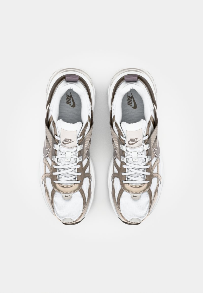 Zapatillas Nike con parte superior de malla en blanco y beige claro. Las características incluyen un cuello acolchado, cordones y un logotipo en la lengüeta y en el talón.