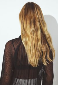 Gennemsigtig sort beklædning med lodrette striber og en åben ryg, der har lange, bølgede blond hår, der falder ned ad ryggen.