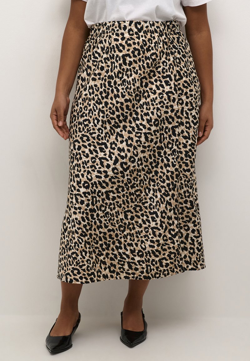 Jupe à motifs léopard en beige et noir. Silhouette en A avec des plis, atteignant le mollet. Portée avec des chaussures noires à bout pointu.