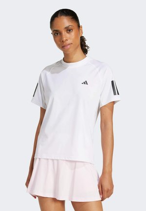 Camiseta atlética blanca de manga corta, con logotipo y detalles en negro. El modelo lleva una falda de tenis rosa en capas.