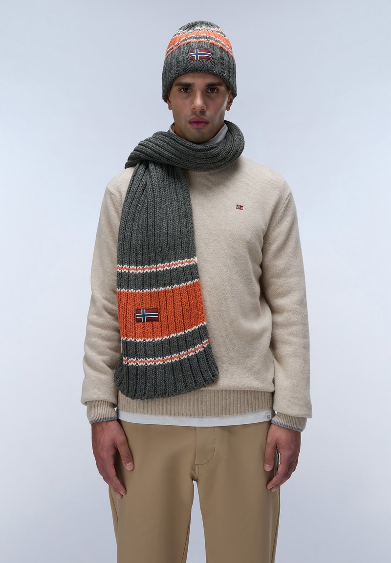 Grå strikket hue og tørklæde sæt med orange og hvide stribe detaljer. Cremefarvet sweater med lille logo design. Beige bukser.