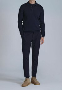 Polo à manches longues côtelé bleu marine associé à un pantalon bleu marine et des chaussures en daim beige, avec un col classique et une patte de boutonnage.