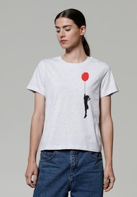 Grijze katoenen t-shirt met een zwarte silhouet van een kind dat een rode ballon vasthoudt, ronde hals, korte mouwen en een ontspannen pasvorm.