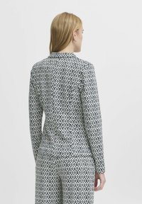 Hladká blůza s vzorem vyrobená z lehké tkaniny. Vyznačuje se diamantovým potiskem v námořnické modři a bílé, s přiléhavým střihem a detaily límečku.