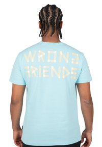 Camiseta de algodón de color azul claro con un corte relajado, que presenta la frase "WRONG FRIENDS" en letras estilo cinta color marrón en la parte posterior.
