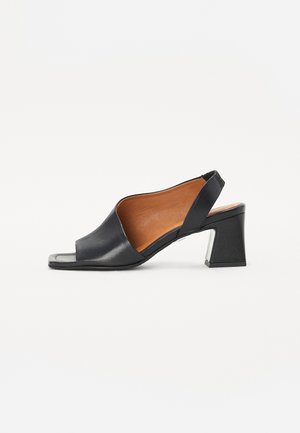 Mocassin slingback noir en cuir verni, ouvert à l'avant avec un talon carré et un intérieur beige. Présente un design supérieur incurvé et une semelle texturée.