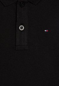 Polo nero con tessuto testurizzato, patta con tre bottoni e logo a bandiera ricamato in rosso, bianco e blu sul petto.