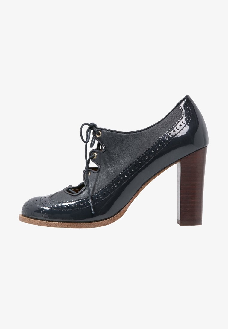 Chaussure en cuir verni noir avec devant lacé, détails brogue, bout amande et talon moyen en bois. Semelle texturée pour une meilleure adhérence.