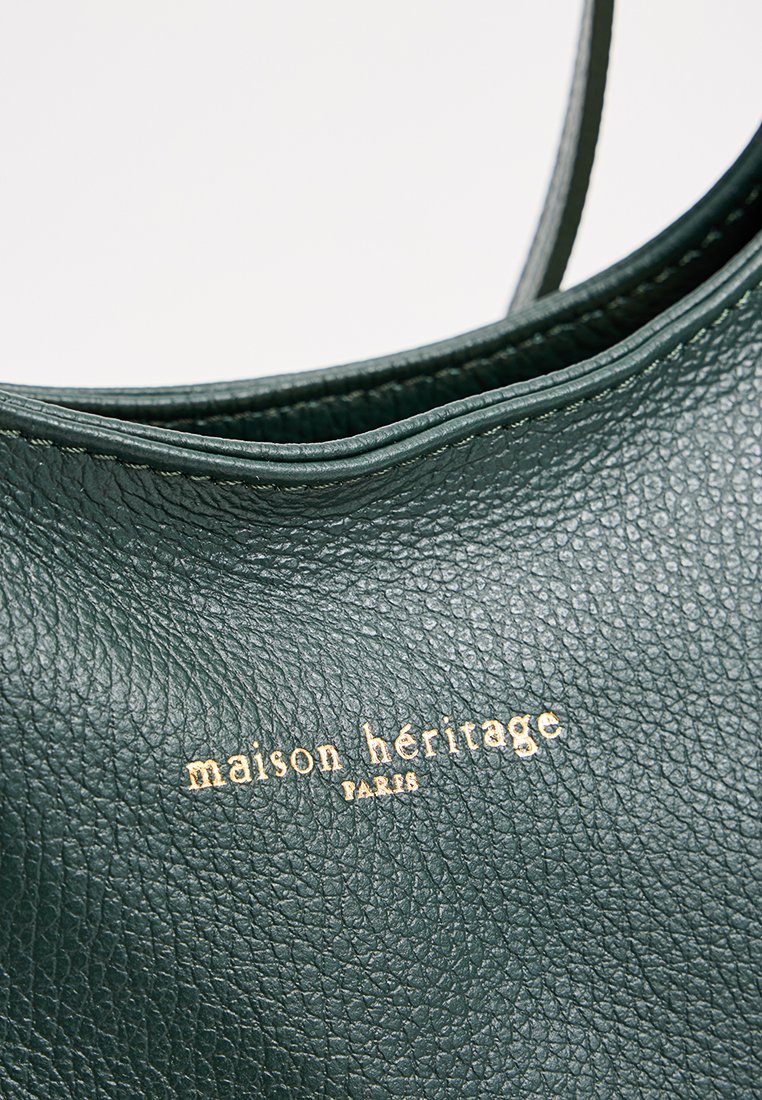 Bolsa de cuero verde texturizado con un borde superior curvado y el nombre de la marca en relieve dorado "maison héritage Paris" expuesto de manera prominente.
