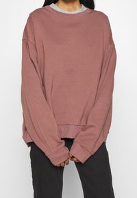 Sweatshirt oversize en rose pâle, avec un col rond et des manches longues. Confectionné dans un tissu doux, avec des poignets et un ourlet côtelés.
