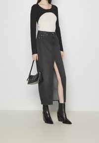 Top de manga larga en negro y crema con un cuello curvado, combinado con una falda de mezclilla oscura de alta abertura y botas de tobillo negras con tacón.