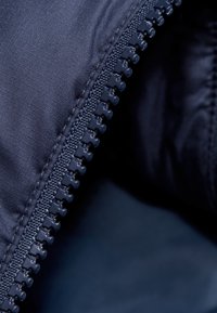 Primo piano di un tessuto blu navy che mette in evidenza una cerniera in plastica con denti interlocking lungo il bordo, enfatizzando la sua texture liscia e il design.