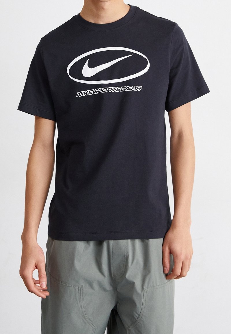 Černé bavlněné tričko s bílým logem Nike a nápisem "Nike Sportswear" uprostřed, krátké rukávy a kulatý výstřih.