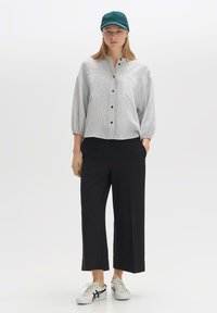 Light grey, textured button-up shirt with puff sleeves and two chest pockets, paired with black wide-leg trousers and white sneakers.