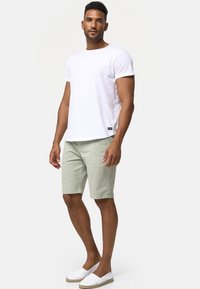 Weißes Baumwoll-T-Shirt, hellgrüne Shorts und weiße Espadrilles. Einfaches Design mit kurzen Ärmeln und dezentem seitlichem Logodetail.