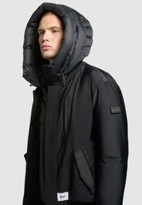 Schwarze Steppjacke mit großer, gesteppten Kapuze, vorderem Reißverschluss und Seitentaschen. Mit einem Markenpatch am Ärmel. Glatte Textur.