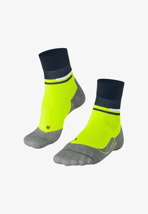 Gelbe und graue Knöchelsocken mit einem gerippten marineblauen Bündchen, die ein gestreiftes Design und ein rotes Logo auf der Unterseite aufweisen.