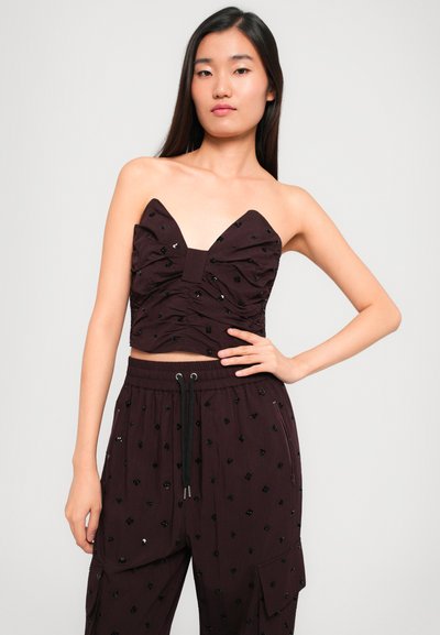 Bordo kratki top s izrezom u obliku srca i nabranim materijalom, ukrašen crnim štrasom. Uparen s odgovarajućim hlačama koje imaju remen s vezicom.