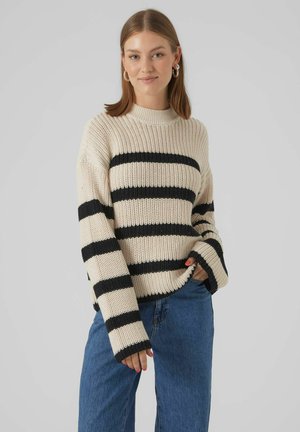 Romantisch gebreid sweater in crèmekleur met zwarte strepen, hoge hals, losse pasvorm en lange mouwen. Gecombineerd met blauwe denim jeans.