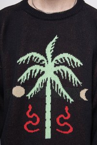 Svart strikket genser med design av et grønt palmetre, røde slanger og beige halvmåne-akkenter. Teksturert stoff med detaljerte mønstre.