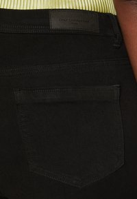 Vaqueros de mezclilla negra con un bolsillo trasero, detalles de costura sutiles y un parche de cuero con el logo "ONLY CARMAKOMA".