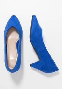 Escarpins à bout pointu en daim bleu avec un talon bloc effilé. Ils présentent une doublure intérieure beige lisse et des détails de couture subtils le long des côtés.