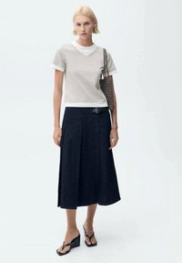 Tricou gri cu mânecă scurtă și decolteu în V, cu tiv alb, asortat cu o fustă tip A din denim închis, cu curea. Sandale negre cu toc wedge și o geantă cu model.