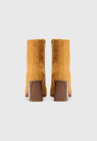 Helle Wildleder-Stiefeletten mit Blockabsatz, mit einem Reißverschluss und vertikalen Nahtdetails an den Seiten.