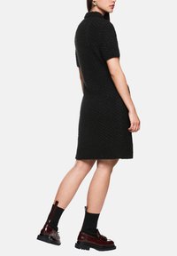 Schwarzes strukturiertes Kleid mit kurzen Ärmeln, knieumspielend. Kombiniert mit bordeauxroten Stiefeletten mit Reißverschluss an der Rückseite und dicken schwarzen Sohlen.