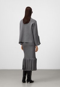 Set di maglione e gonna grigia lavorata a maglia con orlo plissettato, caratterizzato da un fit rilassato e maniche lunghe. Stivali neri fino al ginocchio completano il look.