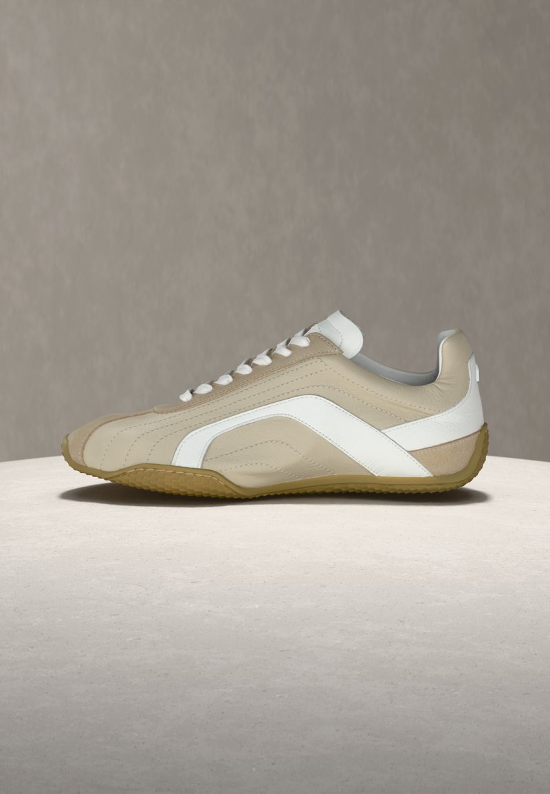 Sneaker en cuir beige et blanc avec des lacets blancs et une semelle gomme, présenté de profil sur une surface claire avec un arrière-plan neutre.