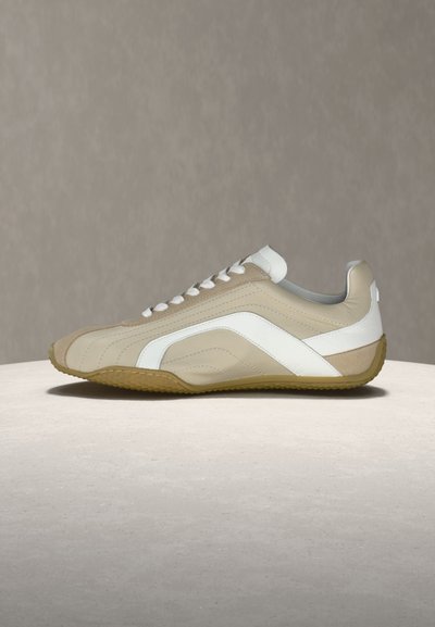 Sneaker en cuir beige et blanc avec des lacets blancs et une semelle gomme, présenté de profil sur une surface claire avec un arrière-plan neutre.
