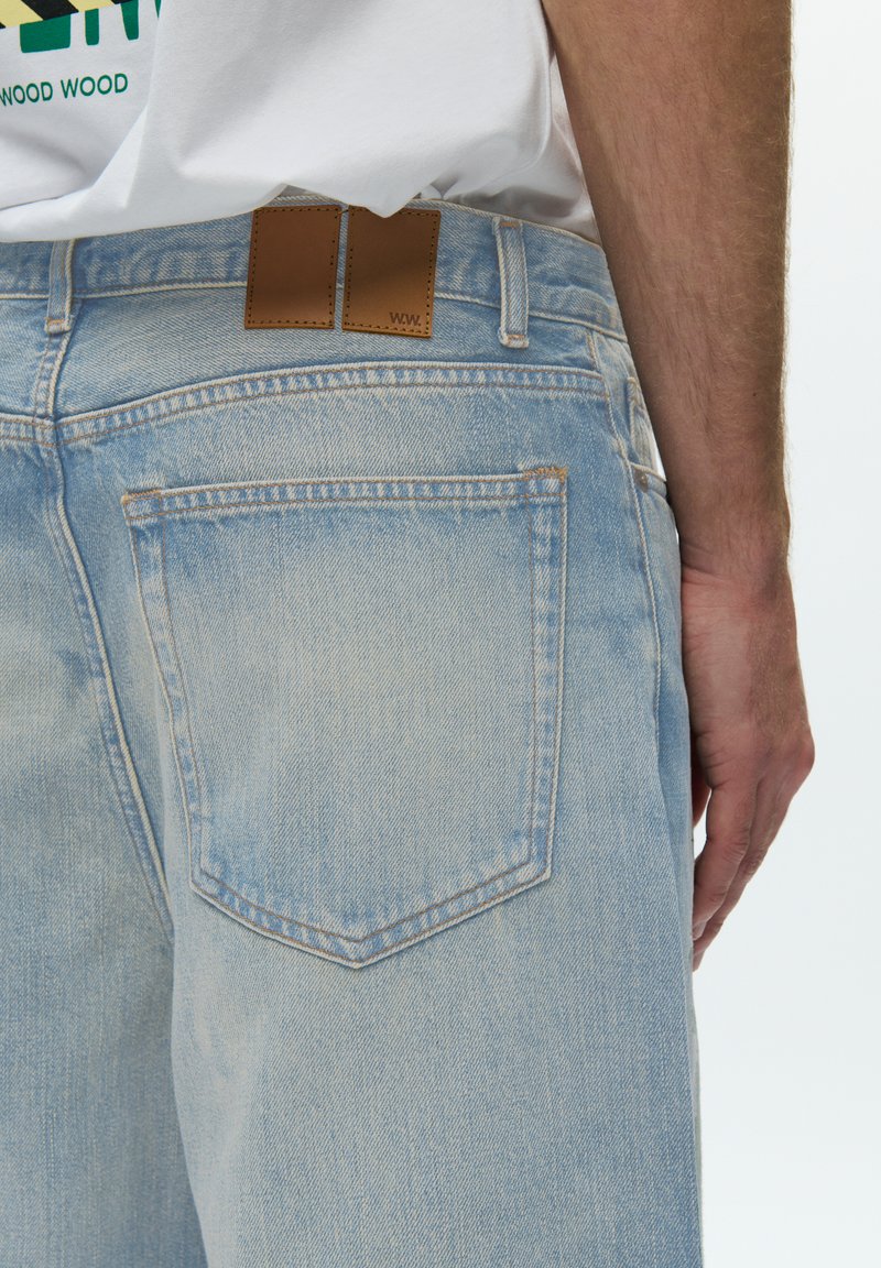 Hellblaue Jeans aus Denim mit verwaschenem Look, zwei Gesäßtaschen und einem braunen Lederetikett mit "WW". Sichtbare Nähte und Texturdetails sind vorhanden.